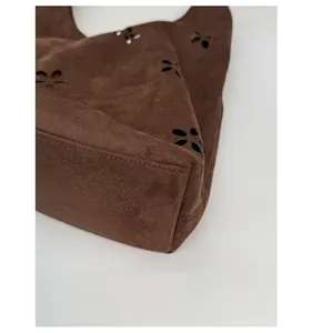 Detail of reinforced corners and laser-cut floral pattern on brown suede tote bag