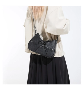Detail of black half-moon shoulder bag with leather bow tie and metal rivets on model
