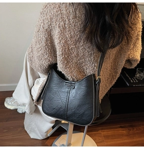 Detail of black textured bucket bag showing the golden metal buckle and wide strap