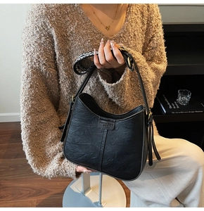 Detail of black saddle bag featuring fashion trend embossing and woven shoulder strap