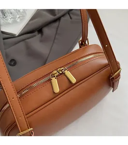 Gros plan du sac baguette en cuir marron avec double fermeture éclair dorée et sangle