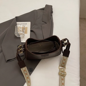 Retro dark brown leather bucket bag with jacquard strap on a grey suit and art book