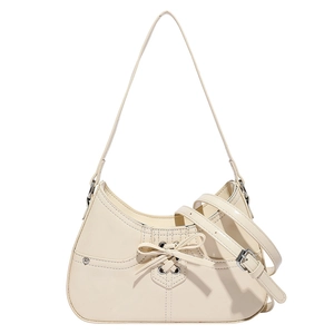 Cream patent leather hobo bag with ribbon bow and silver eyelets on white background
