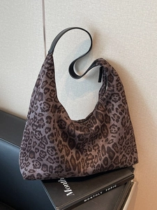 Large leopard print faux suede tote bag with black leather shoulder straps on a sofa