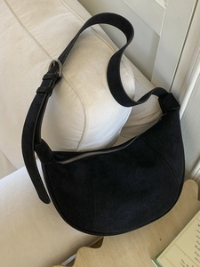 Vintage matte black hobo bag with adjustable wide strap on a white fabric surface