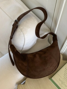 Deep brown frosted suede crescent bag with vintage adjustable strap on white sofa