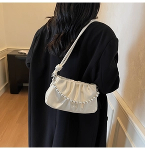 Détail du sac nuage plissé crème avec chaîne en perles sur un blazer noir