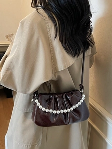 Sac nuage plissé en cuir verni marron foncé avec chaîne en perles porté à l'épaule
