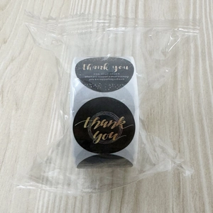 Detail of black round Thank You stickers roll with gold foil lettering in plastic wrap