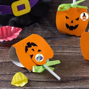 Orange Halloween pumpkin lollipop card holder with green ribbon bow on a dark wooden table
