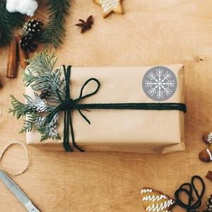 Round Christmas snowflake stickers in grey and white on kraft gift boxes for holiday packaging