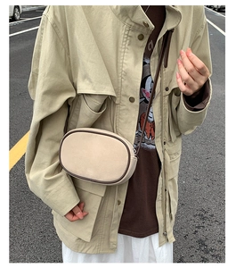 Detail of vintage suede oval crossbody bag with brown piping on model in street setting