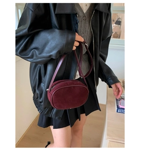 Close-up of a burgundy suede oval crossbody bag with top zipper and fine shoulder strap