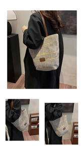 Detail of plaid tote bag with brown leather straps shown on shoulder in a cozy home setting