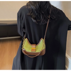 Detail of green suede moon bag with brown leather trim and gold buckle on a black coat