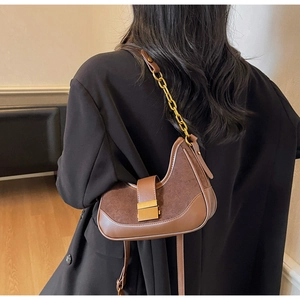 Detailed shot of brown suede crescent bag with gold buckle and chain shoulder strap