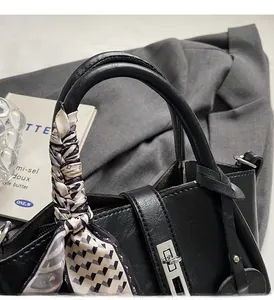 Detailed close-up of a black leather bucket bag with a silk scarf handle and silver lock