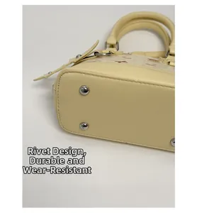 Detail view of four protective metal studs on the base of a cream shell-shaped handbag