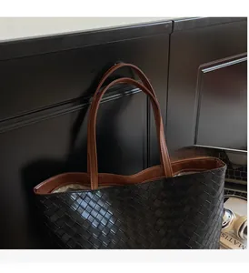 Detail of black woven leather tote bag featuring brown shoulder handles and spacious design