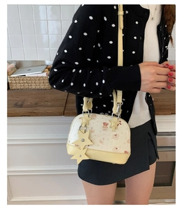 Detail of beige shell bag with cartoon bear prints and yellow star pendants on model