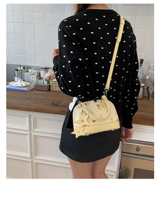 Detail of shell-shaped handbag showing cute bear print and star charm on beige PU leather