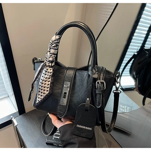 Détail d'un sac seau en cuir noir avec fermoir rotatif argenté et foulard en soie