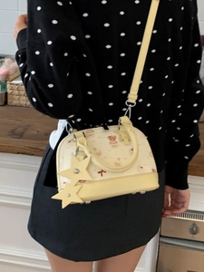 Beige shell bag with bear print and yellow handles worn as a crossbody shoulder bag