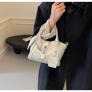Détail d'un sac seau crème avec boucle argentée et poignée ornée d'un foulard stylé