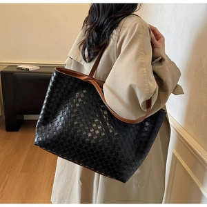 Close-up of woven leather tote bag with brown handles on model in a minimalist room