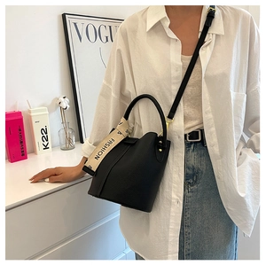 Détail du sac seau noir en cuir grainé avec ruban de mode porté par un mannequin