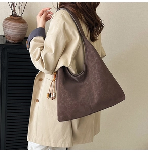 Detail of dark brown matte leather hobo bag with wooden bead charm and elegant draping effect