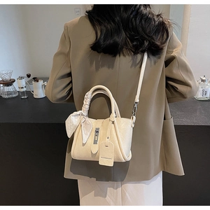 Chic cream bucket bag with decorative silk scarf and metal buckle shown in cafe setting