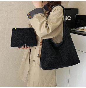 Close-up of black suede tote bag and matching clutch set worn by a model in a studio