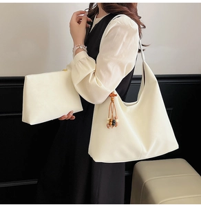 Detail of off-white tote bag with a bead tassel and matching pouch on a model