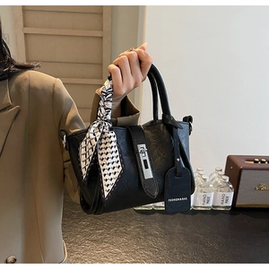 Détail du sac seau en cuir noir avec fermoir rotatif argenté et foulard à carreaux