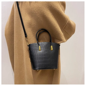 Detail of black stone-textured bucket bag with gold hardware on earth-tone coat