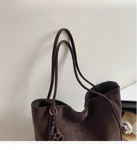 Detail of dark brown faux suede tote bag with stylish decorative metal and woven charm