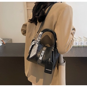 Détail du sac seau en cuir noir avec fermoir argenté et décoration de foulard en soie