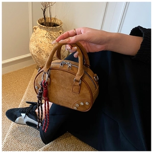 Détail du sac bowling en daim vintage avec clous métalliques et pompon bohème tissé