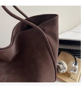 Detail of dark brown tote bag with vintage leather texture beside laptop and book