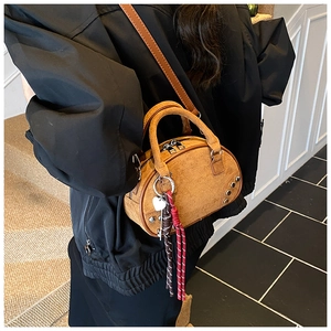 Détail du mini sac bowling en daim fauve avec clous et breloque porté par un mannequin