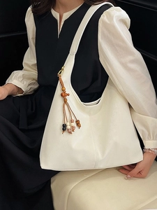 Minimalist white leather tote bag with artistic beaded charm shown in a model side view