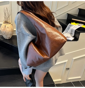 Borsa hobo in pelle marrone lucida indossata da una modella in un interno minimalista