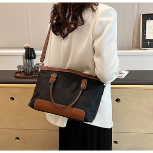 Rear view of a black nylon tote bag with brown leather trim styled for urban commuting