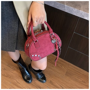 Vue détaillée d'un sac bowling bordeaux clouté avec pendentif coeur et sangle à carreaux