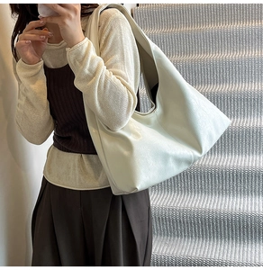 Dettaglio borsa hobo in morbida pelle crema indossata da modella su una scala