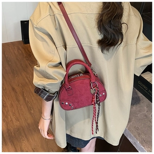 Détail du sac bandoulière rouge semi-circulaire avec breloque cœur et pompons tissés sur l'épaule