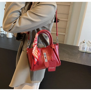 Détail du sac seau en cuir rouge avec fermoir métallique et foulard à carreaux
