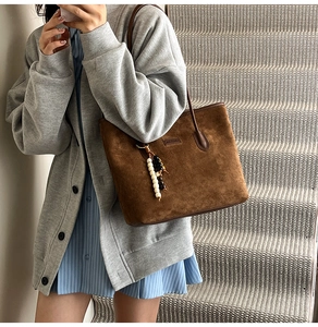 Detail of brown suede tote bag with stylish beaded pendant and minimalist brand tag