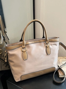 Beige tote bag with brown leather trim and shoulder strap on a black display stand